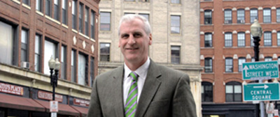 Joseph Mulligan, a Transformative Development Fellow at MassDevelopment, stands at the confluence of three different types of architecture in Lynn’s Central Square.
