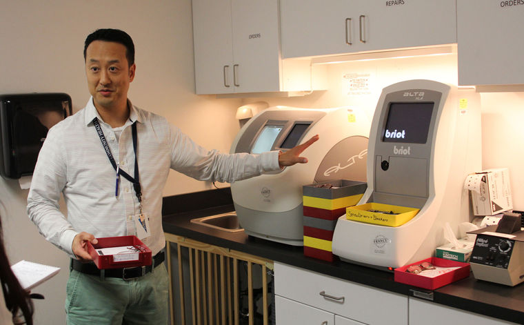 Steve Yoon, an optician at Lynn Community Health Center, shows off an eyeglass-making machine.